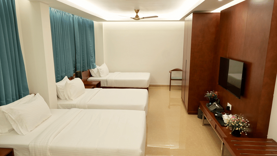 A Deluxe Quadruple Room at Le Royale Palace featuring four single beds, a flat-screen TV, and elegant wooden furnishings