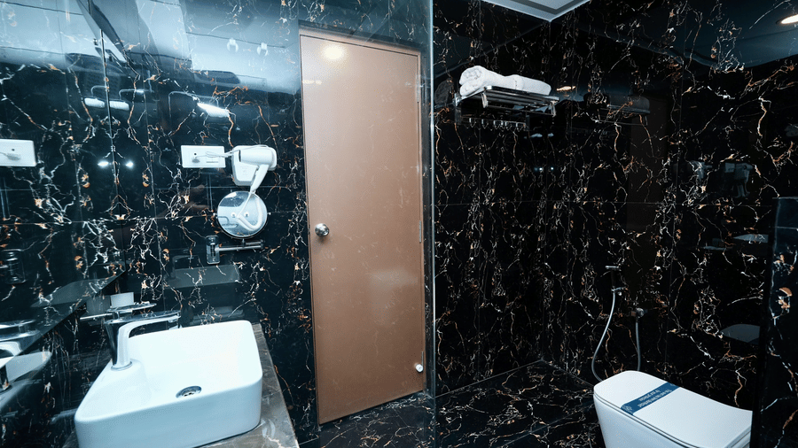 A bathroom in the Deluxe Quadruple Room at Le Royale Palace with black marble walls, modern fixtures, and a glass shower area