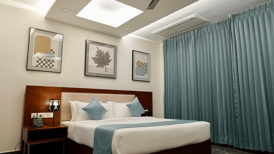 A bedroom in the Majestic Suite at Le Royale Palace featuring a king-size bed, soft blue curtains, and elegant wall art