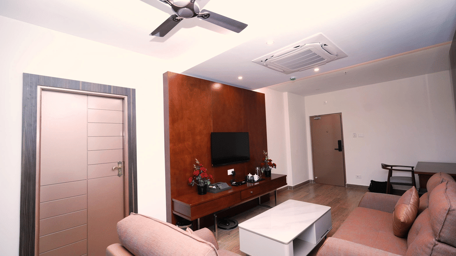 A view of the Majestic Suite living area at Le Royale Palace showcasing modern furnishings, wall-mounted TV, and ample space for relaxation