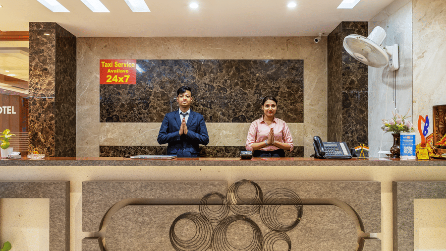 2 reception staff standing behind a dark marble lobby desk, wearing formal attire and welcoming guests with a respectful traditional gesture of greeting at Hotel Corporate Suites