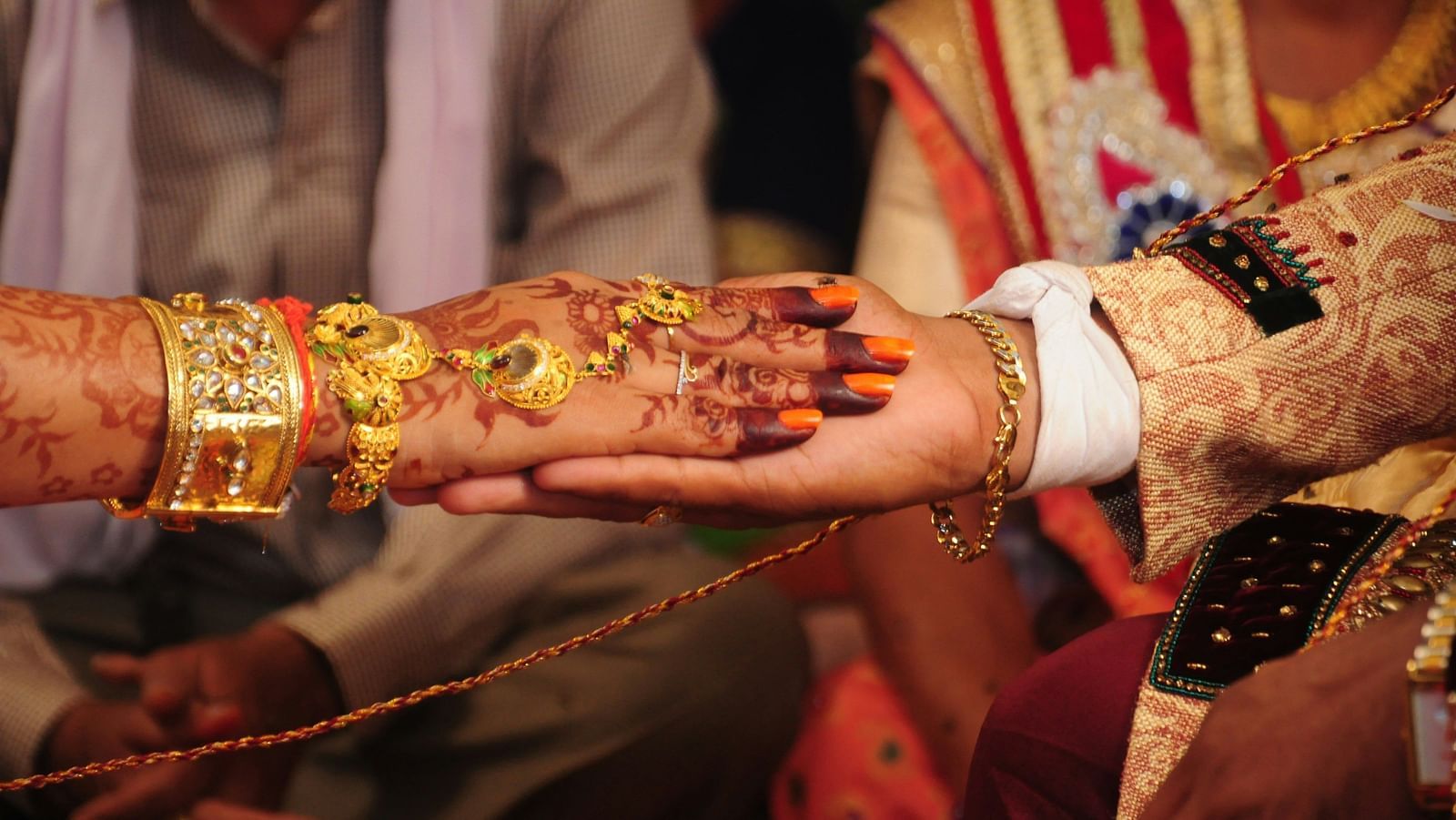This image captures a close-up of a traditional Indian wedding ceremony. The bride and groom's hands are clasped together