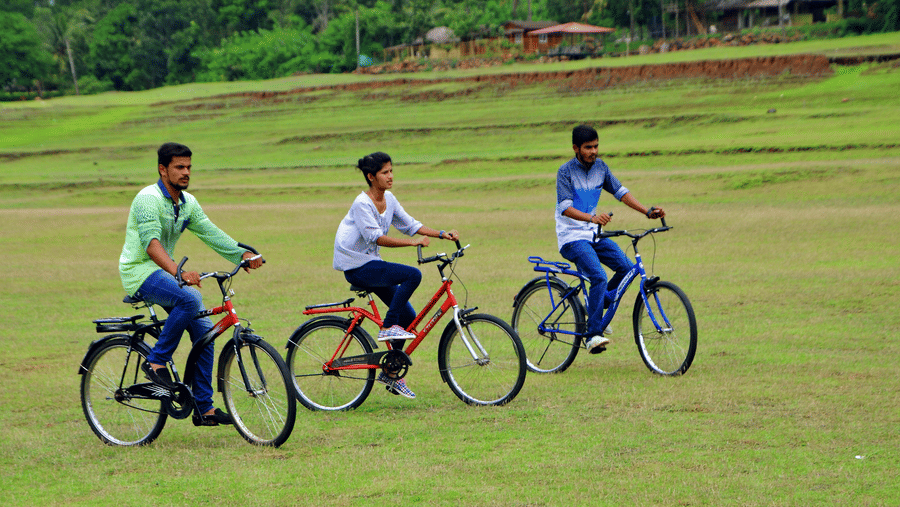 Image of three people cycling in an open area with trees in the background at Coorg Jungle Camp Backwater Resort, Kushalnagar.