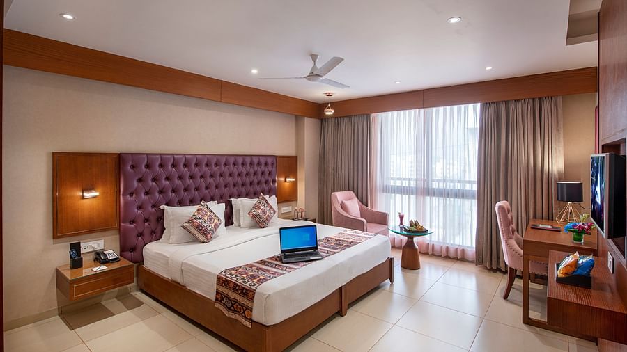 A spacious hotel room with a large bed, seating area, and city views - SK Lords Inn Ahmedabad