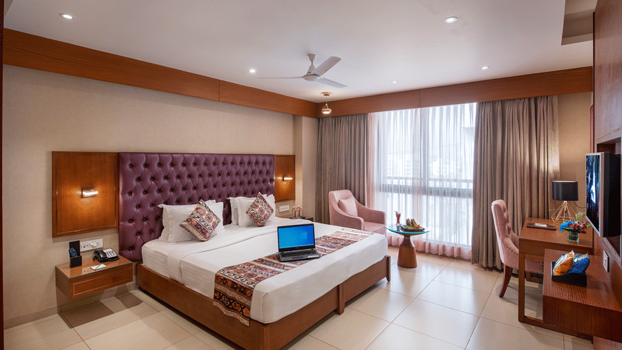 A spacious hotel room with a large bed, seating area, and city views - SK Lords Inn Ahmedabad