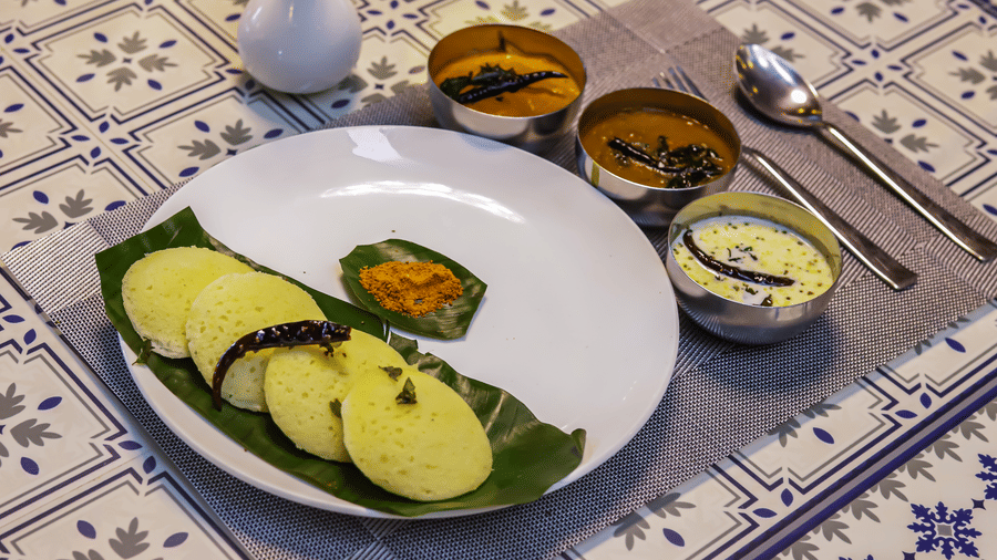 A white plate with food, accompanied by small bowls of sauces, rests on a patterned table at Vedikant Resorts The Mallard Corbett.