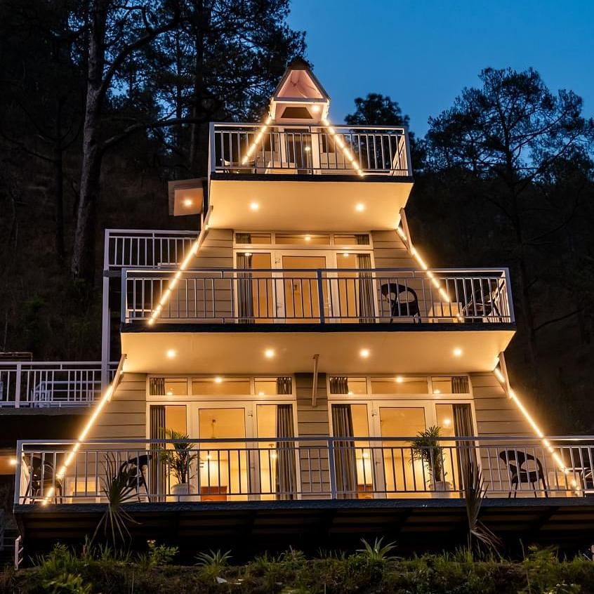 A front view of an illuminated A-frame building at dusk, with lights glowing from within and around it.