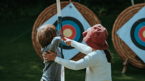 A parent teaching archery to a child on the lawns of The Manor Luxury Apartments, Shimla, promoting family bonding.