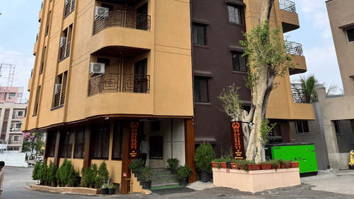 A facade of a building with a large tree in front at VITS Select Kharadi, Pune.