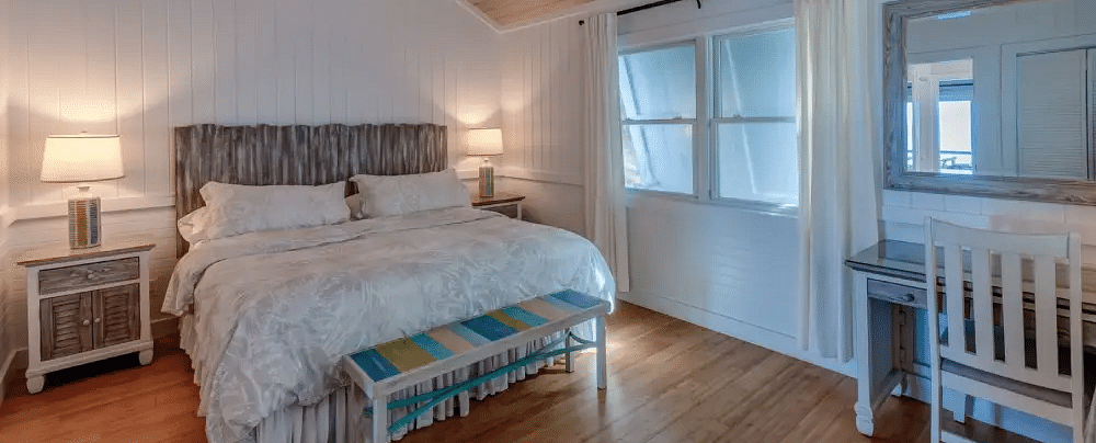 Bright bedroom with a double bed, ceiling fan, white walls, and a baby crib placed near the window in a guesthouse | Abaco Inn