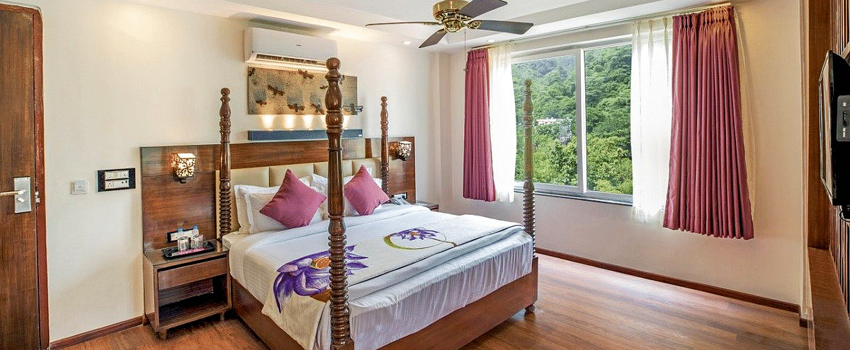 A comfortable double bed with a ceiling fan right above it on a false ceiling and a window besides it at Regenta Inn DLS.
