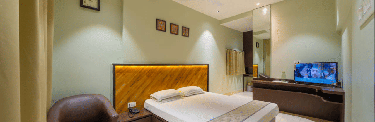 Minimalist bedroom featuring a double bed, wooden headboard, a seating area, and a TV on a wooden cabinet – Hotel Dolphin Puri