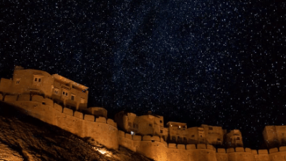 Jaisalmer Fort is illuminated at night with a starry night sky above, in Rajasthan, India.