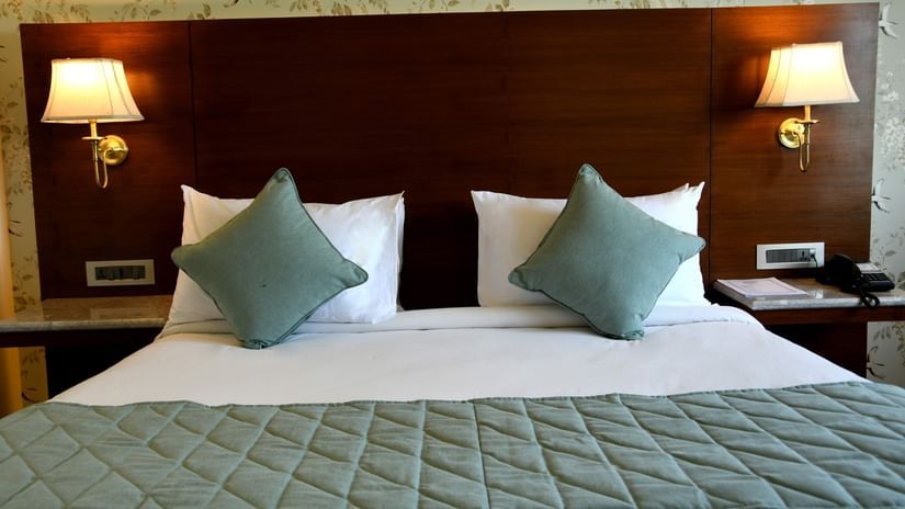 Premium - Chir Tree View at Mastiff Villa Camellia, Palampur featuring a plush bed with a pillows and a couple of cushions along with a bed runner and two lamps mounted on the wall over the nightstands on both sides