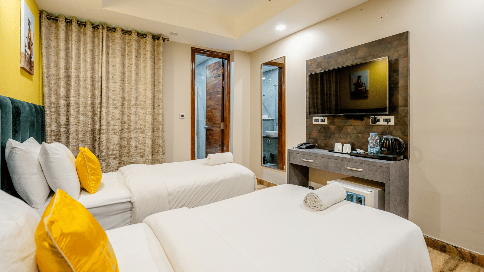 A bedroom at Lime Tree Hotel Near Medanta–The Medicity, Gurgaon featuring twin beds, a flat TV screen, a cabinet table with tea and coffee maker, a minibar, and an attached bathroom.
