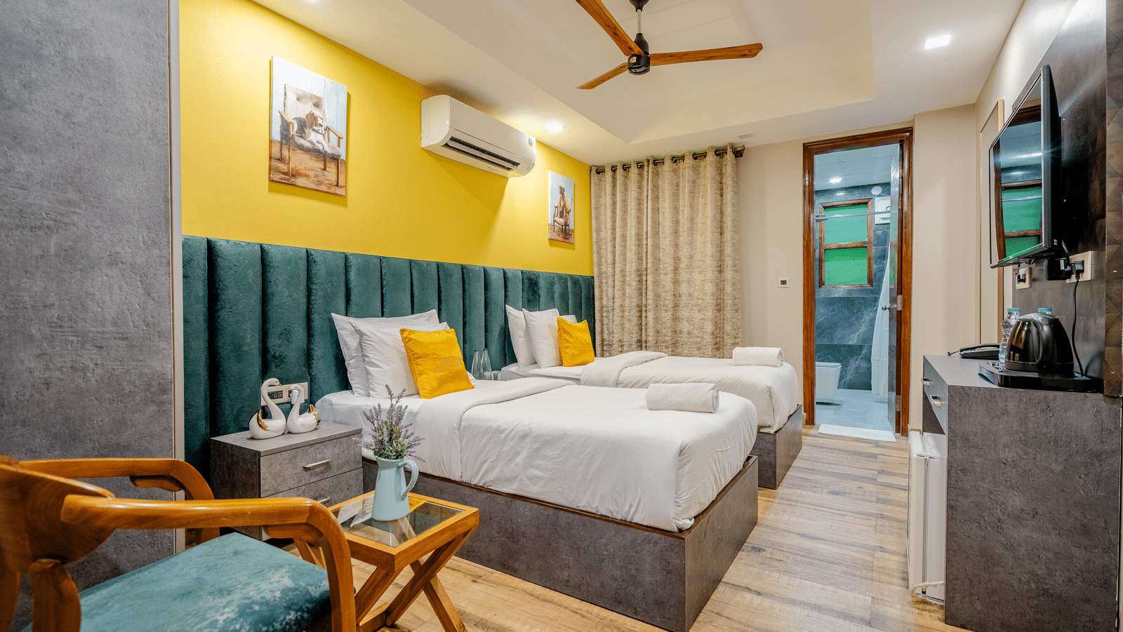 A room at Lime Tree Hotel Near Medanta-The Medicity, Gurgaon featuring two beds, a cabinet table, a chair and centre table, tea and coffee maker, a flat TV screen, an AC, and an attached bathroom.