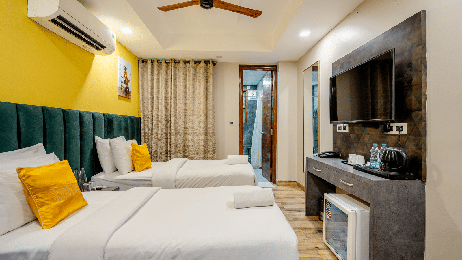 A room at Lime Tree Hotel Near Medanta-The Medicity, Gurgaon featuring two similar looking beds, a minibar, cabinet tabel, a flat TV screen, an AC, and an attached bathroom.