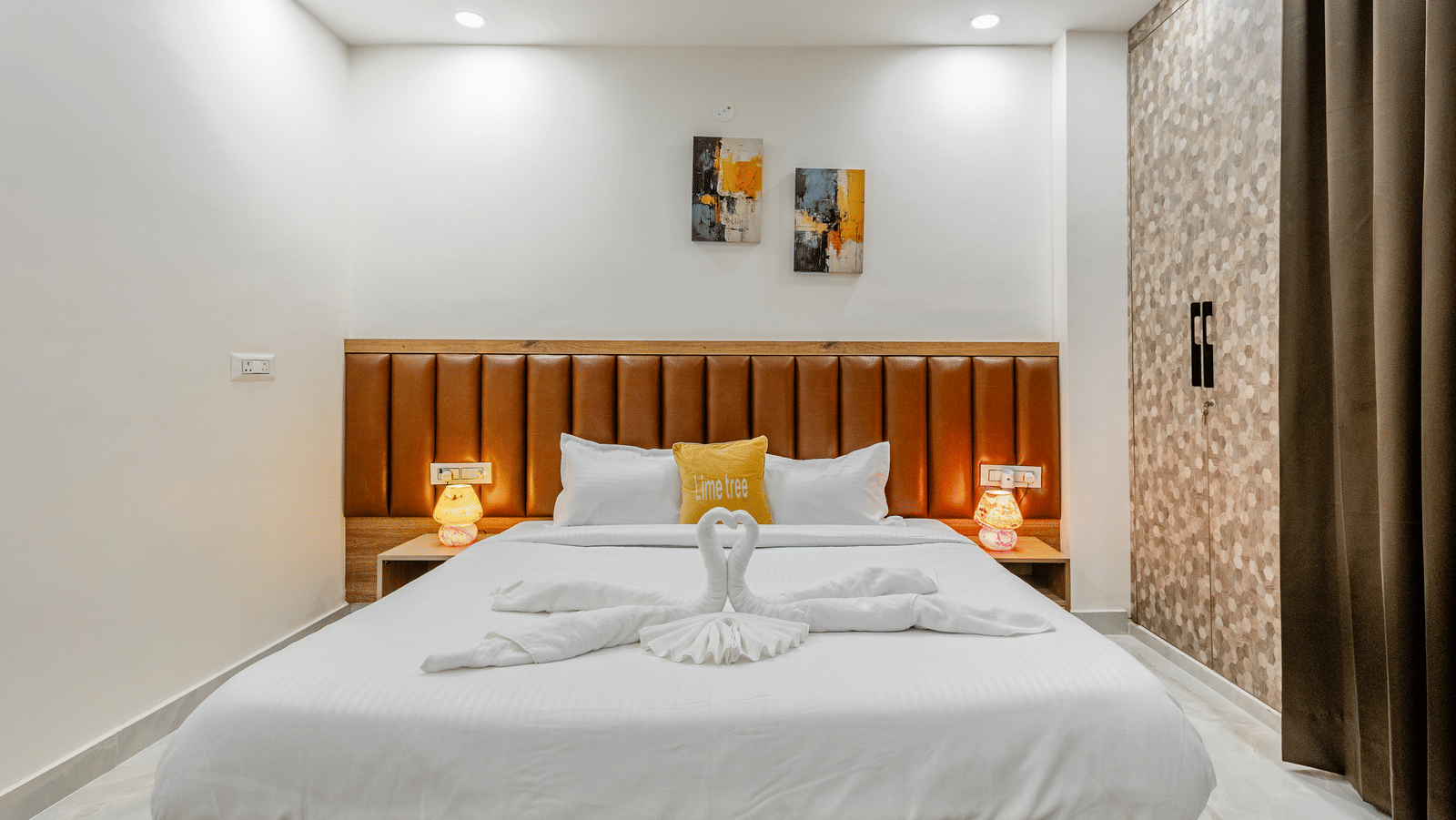 Bedroom of Lime Tree Hotels & Service Apartment Private Limited featuring a wooden panelled headboard, bedside lamps, and framed wall art.