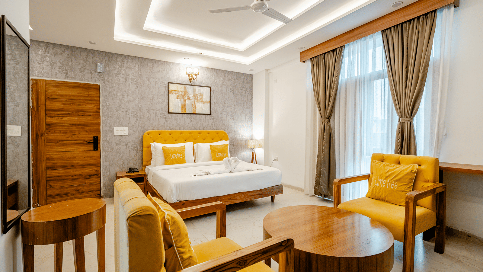 Bedroom of Lime Tree Hotels & Service Apartment Private Limited featuring a bed, a round wooden table, and yellow armchairs by the window.
