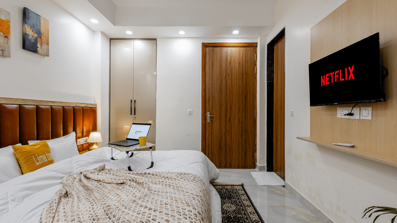 Bedroom of Lime Tree Hotels & Service Apartment Private Limited featuring a wooden panelled headboard, a study desk, and a wooden wardrobe.