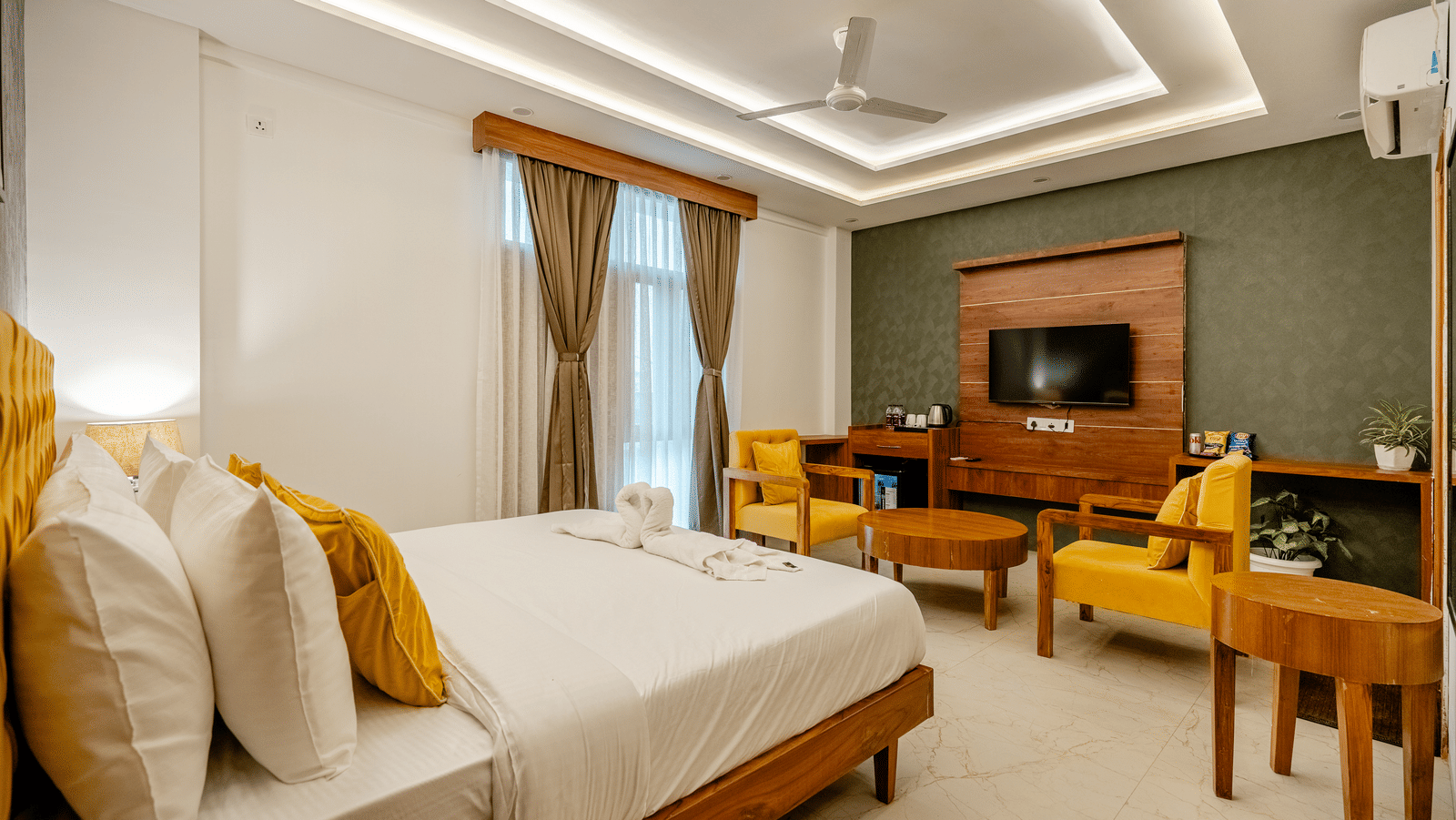 Bedroom of Lime Tree Hotels & Service Apartment Private Limited featuring a bed with yellow cushions, a television console, and yellow armchairs.