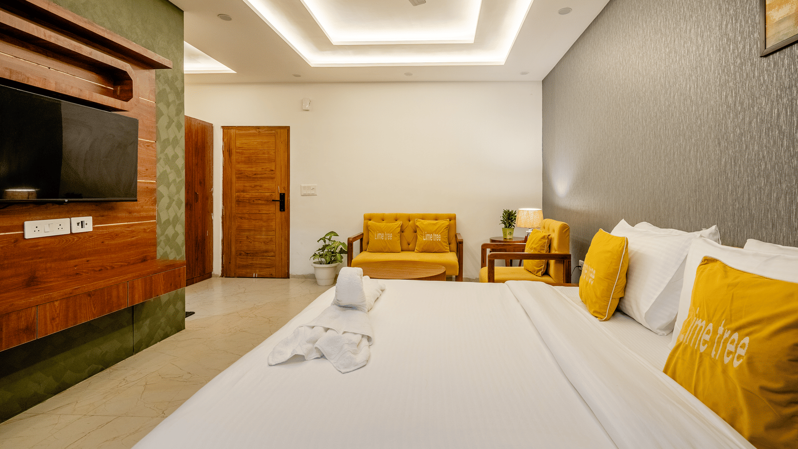 Bedroom of Lime Tree Hotels & Service Apartment Private Limited featuring a bed with folded towels, a wall mounted television, and a wooden wardrobe.