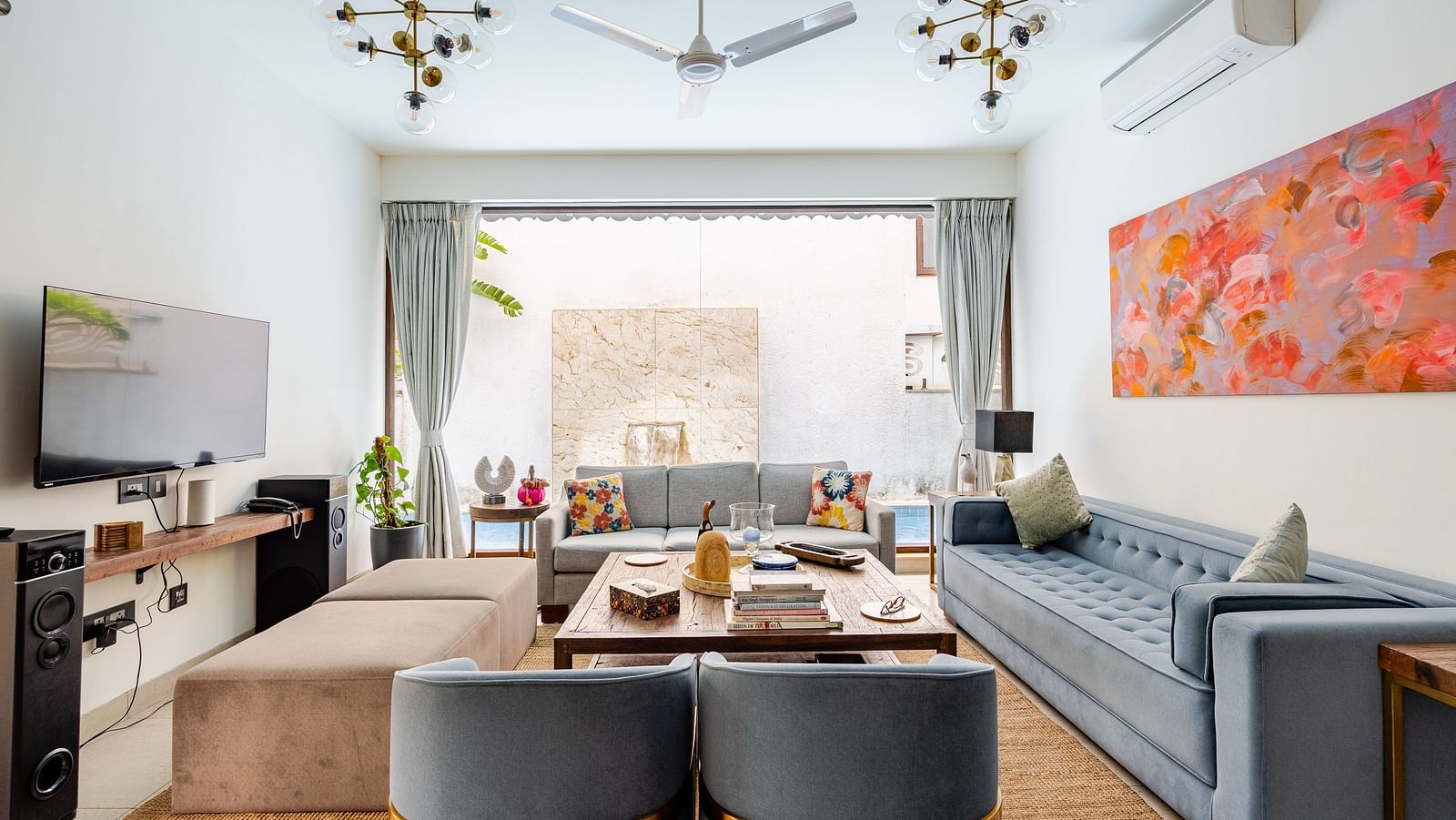 Living area at Lindsay Manor with a grey sofa set, TV, ceiling fan, abstract wall art, and an open view to an outdoor space.