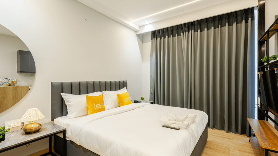 Bedroom with a grey upholstered headboard, yellow cushions, a round mirror and full-length curtains at Street Studio