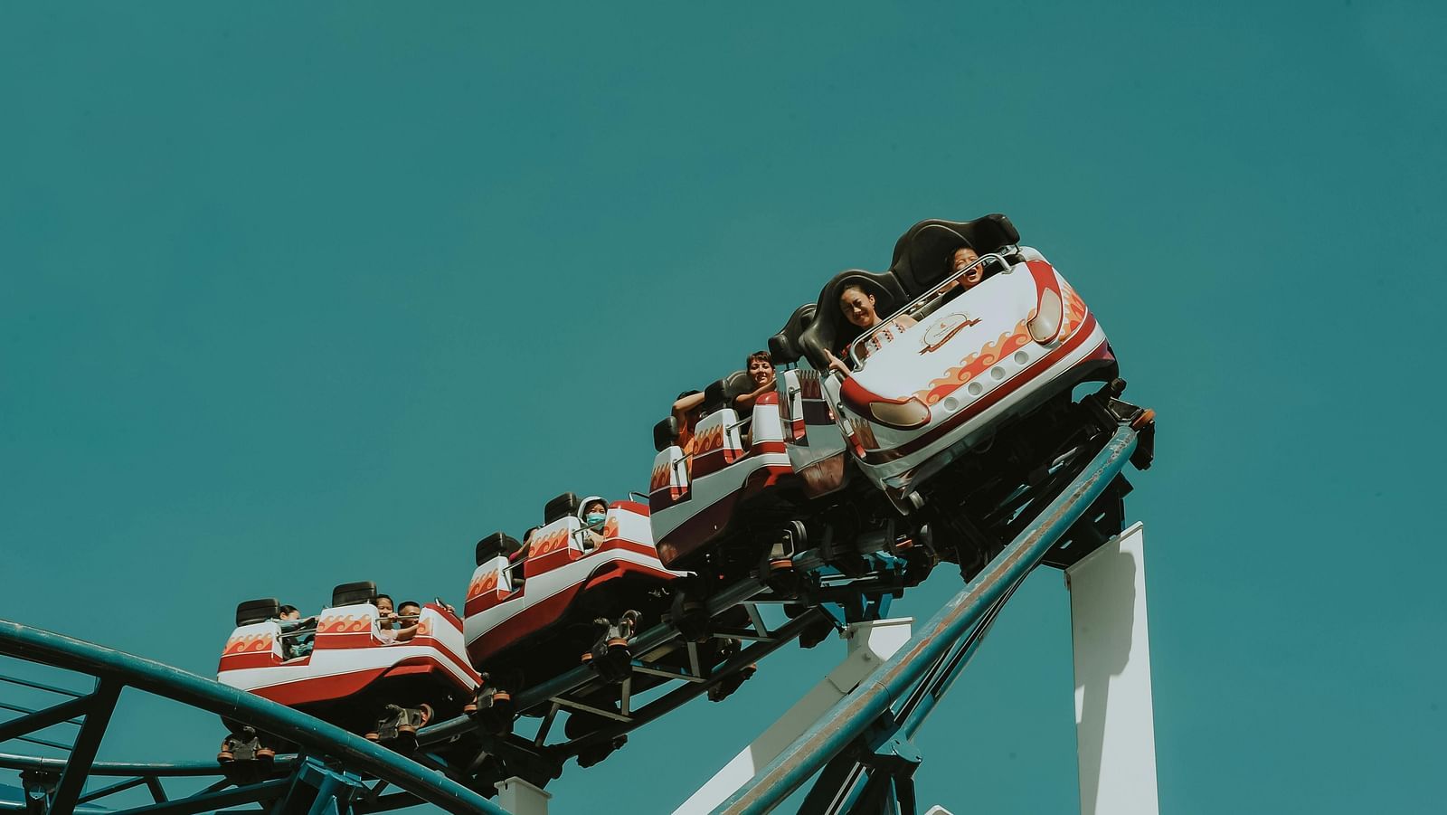 A roller coaster filled with thrilled riders ascends against a clear blue sky
