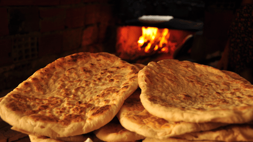 Stack of freshly baked traditional bread near a clay oven.