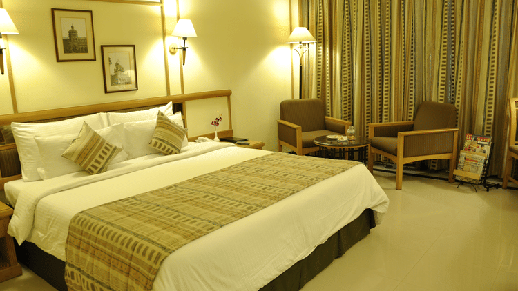 Executive Room at Aditya Park Hyderabad, featuring double size bed, a seatijng area with chairs and centre table, and lamps.