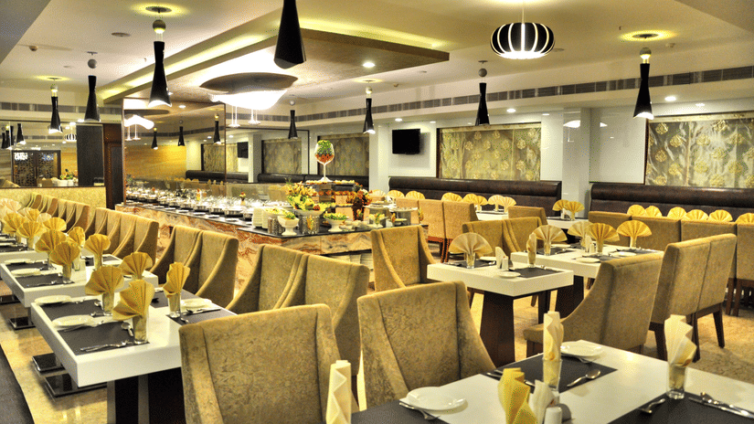 A spacious and elegantly lit restaurant with plush seating, neatly set tables, and a buffet counter – Raj Park Hotel in Alwarpet, Chennai
