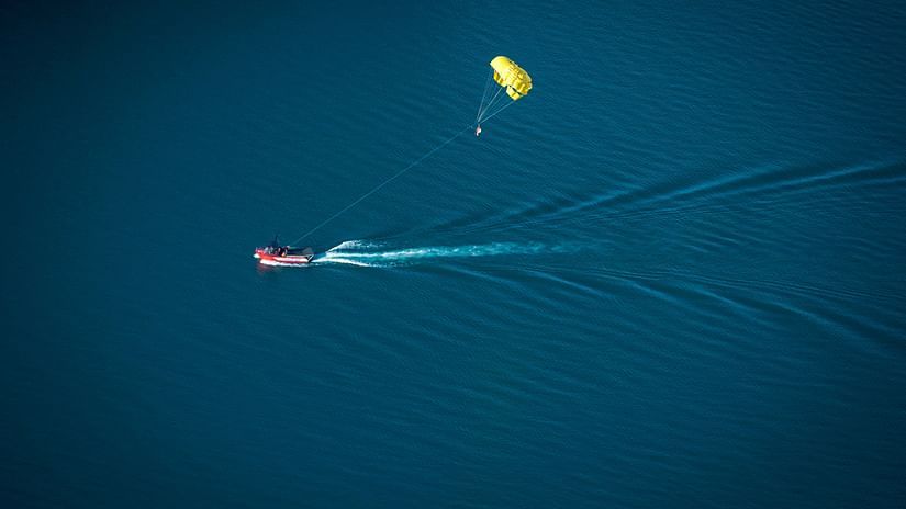 a speed boat travelling on the waterbody, parasailing with a person being hung on it 