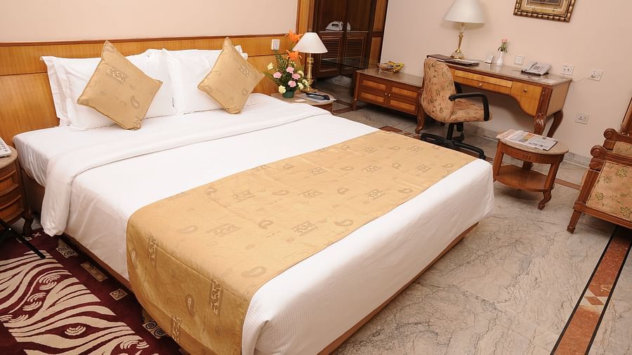 a double bed with side tables and a study table on the side inside one of the rooms - Raj Park Hotel, Chennai