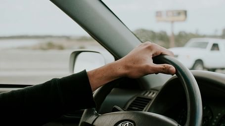 A close up shot of a person holding a steering wheel while driving on the road.