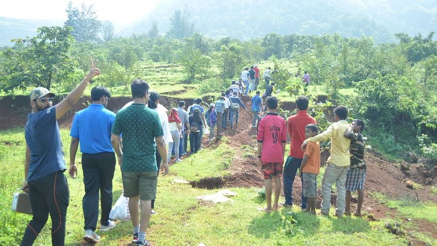 Guests at Forest Escapes Koyna participate in an outdoor activity on a grassy field with hills in the distance.