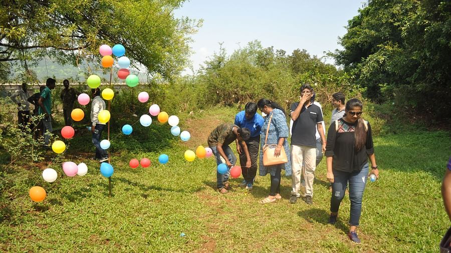 A group enjoys an outdoor event at Forest Escapes Koyna, with colorful decorations in the background.
