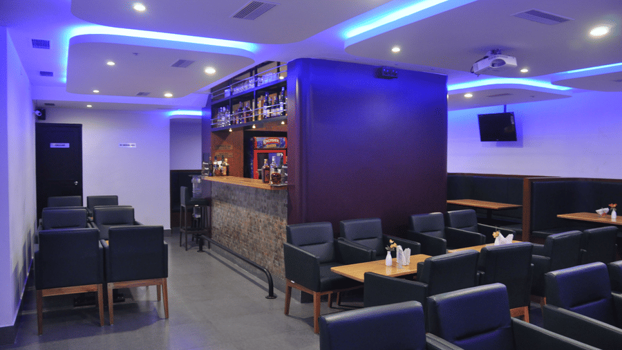 A modern dimly lit hotel bar lounge area with black leather armchairs and vibrant blue LED ceiling lights - Hotel Pandian