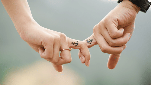 Two hands with matching anchor tattoos on their fingers holding eachother's index fingers