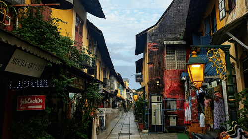 A narrow, cobbled street with colourful, tall timber-framed buildings and shops under a cloudy sky.