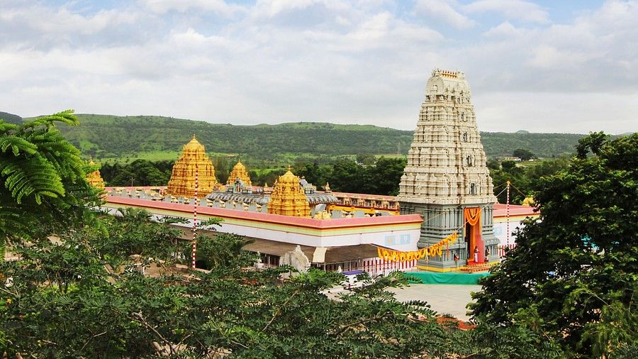 South Indian temples surrounded by trees and hills. Above them is an open sky.