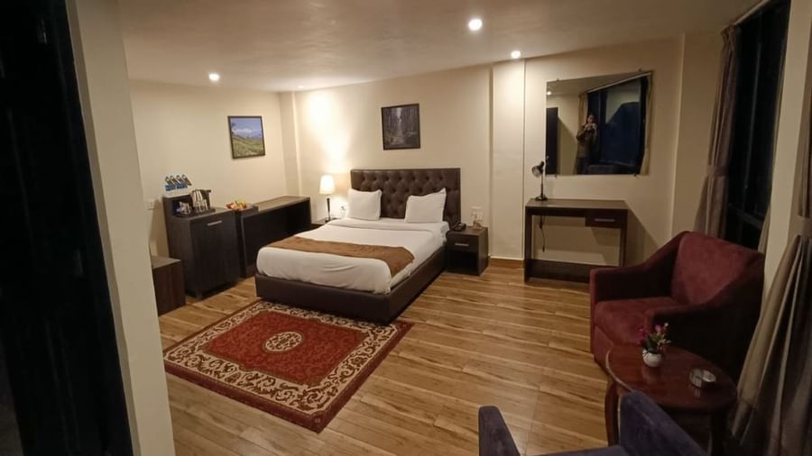 Semi Deluxe room at Istana Resort and Spa by Sagar featuring a queen size bed, sofa chairs, a table, and a cabinet with tea and coffe maker.