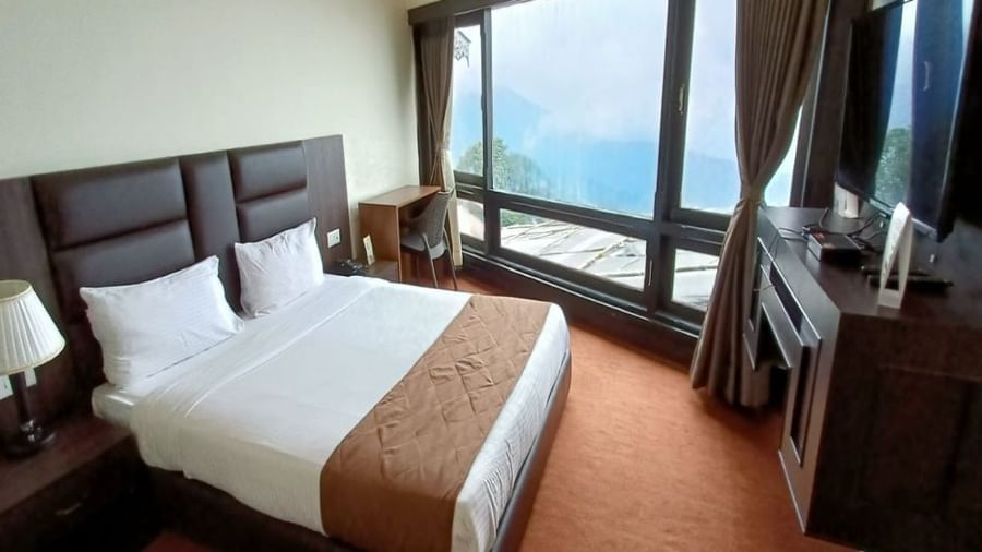 Semi Deluxe room at Istana Resort and Spa by Sagar featuring a queen size bed, a flat TV screen, and a large window with curtains withdrawn.