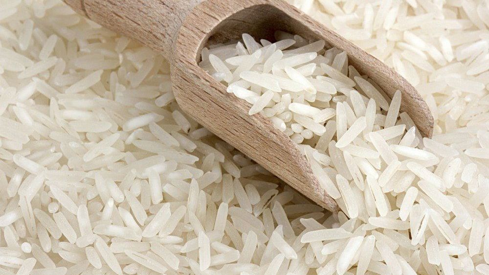 Close-up of white pusa basmati rice with a wooden scoop resting on top.