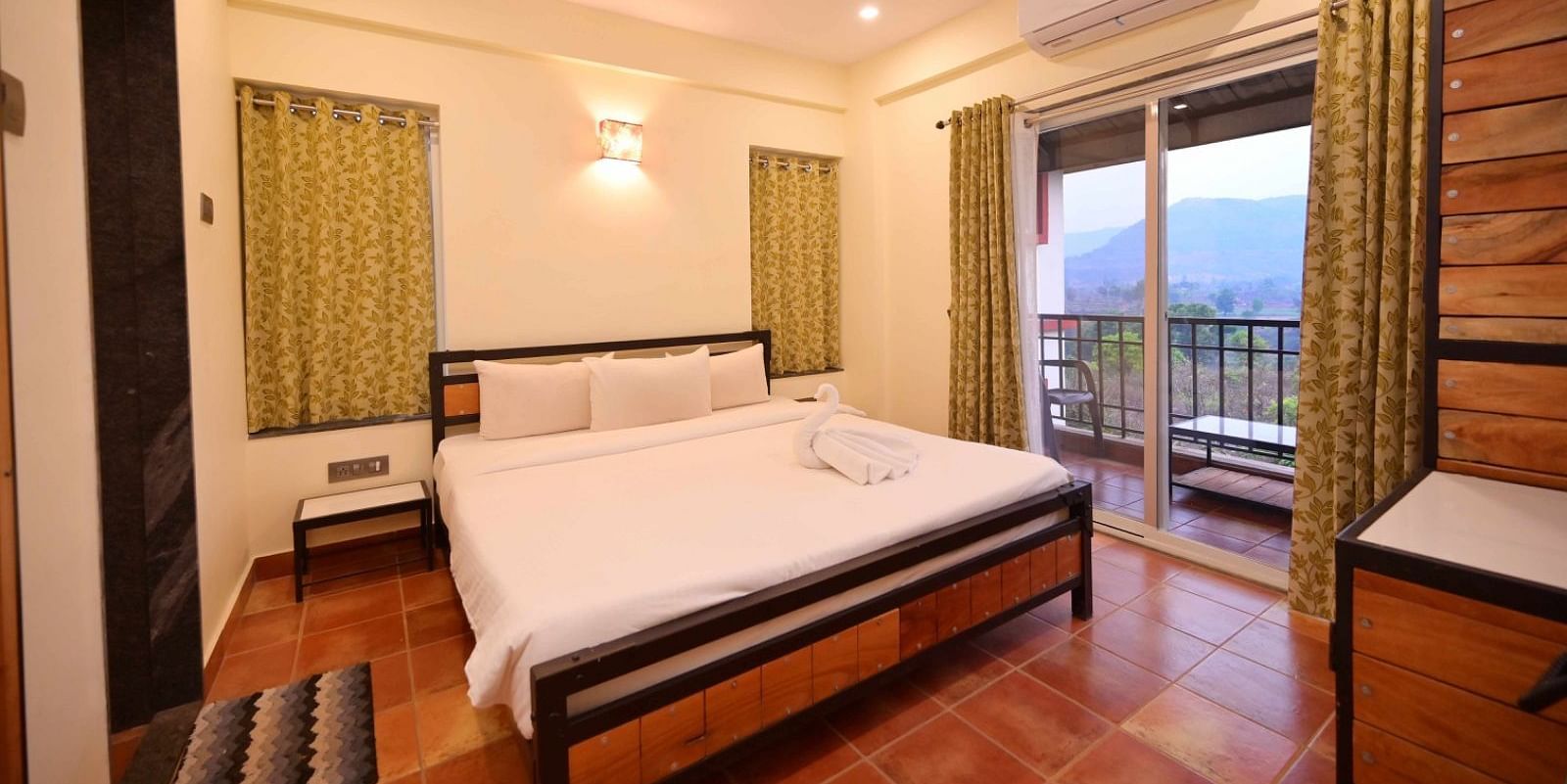 A bedroom with a wooden bed frame, white linens, a ceiling fan, an air conditioner, and a sliding glass door leading to a balcony with a view.
