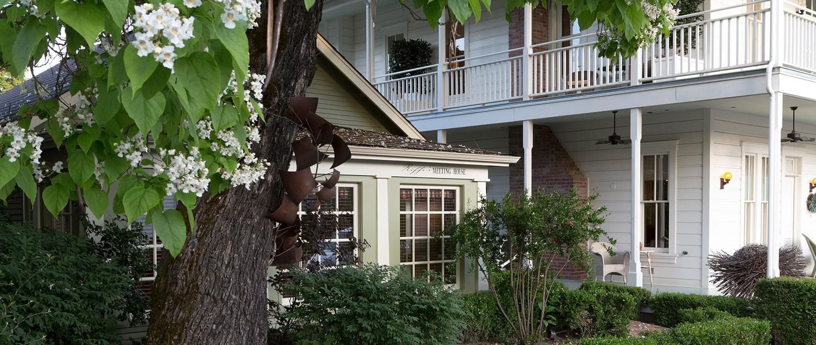 A view of Tallman Hotel partially shaded by a tree and surrounded by bushes