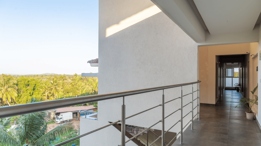 A balcony with metal railings with a door in the front and a wide view of the city with green surroundings at Amara Grand Baga, Goa.