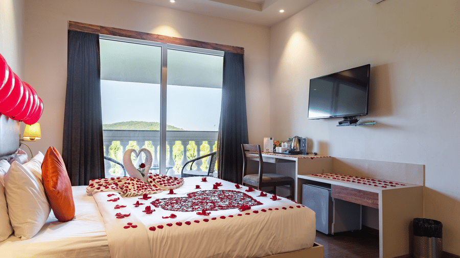 Side view image of a room with a bed and flower petals arranged on the bed and a television in front at Amara Grand Baga, Goa.