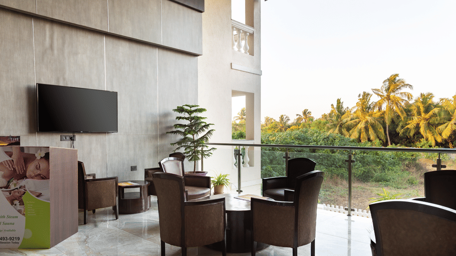 Seating area with tables and chairs and a wall-mounted TV at Amara Grand Baga, Goa.