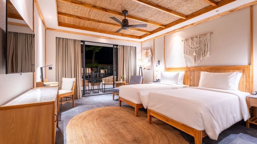 A hotel room with 2 beds, a ceiling fan, a TV, and a balcony at Royal Tulip, Chitwan.